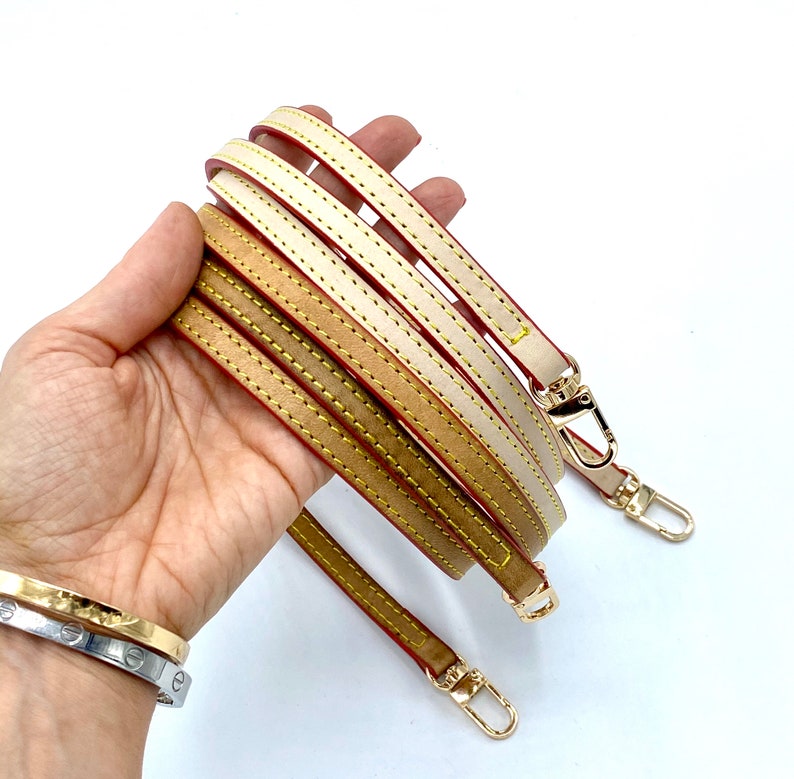 May include: Three leather straps with gold hardware and red stitching. The straps are beige, brown, and cream.
