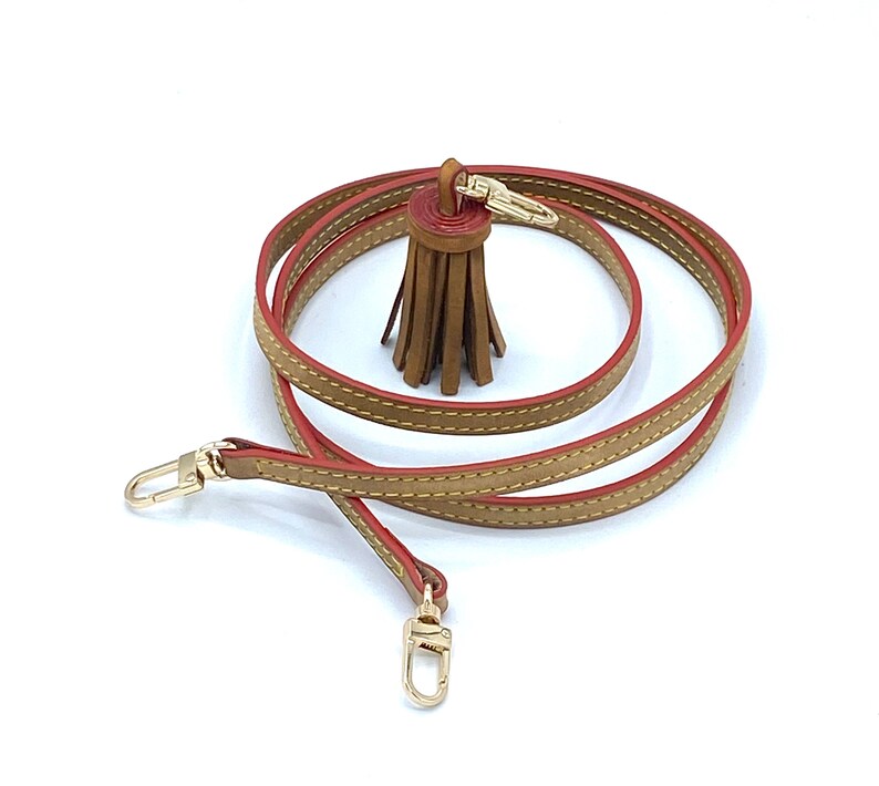 May include: A brown leather strap with red stitching and a brown leather tassel. The strap has gold-toned hardware and is approximately 50 inches long.