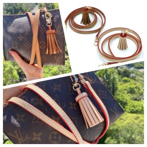 May include: A brown and tan leather handbag with a red stitch detail and a beige tassel. The bag has a gold chain strap and a gold clasp.