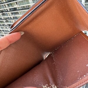 May include: Open brown leather wallet with visible wear and tear. The interior features multiple compartments and a worn, textured surface. The wallet is held open, revealing its inner structure and signs of use.