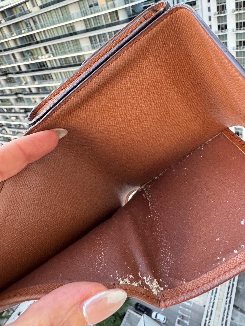 May include: Open brown leather wallet with visible wear and tear. The interior features multiple compartments and a worn, textured surface. The wallet is held open, revealing its inner structure and signs of use.