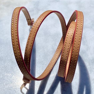 May include: A brown leather strap with red stitching. The strap is folded in half and has a gold metal clasp.