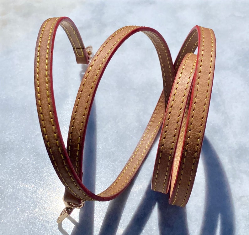 May include: A brown leather strap with red stitching. The strap is folded in half and has a gold metal clasp.