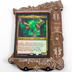 May include: A wooden card display frame with a Magic: The Gathering card featuring Omnath, Locus of Rage. The card is green, red, and white with a green and red creature on it. The frame has a dial on the side with numbers 0-9.