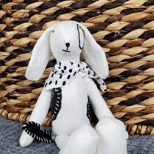 May include: White fabric bunny rabbit toy with black and white polka dot scarf. The bunny has black eyes and a black nose.