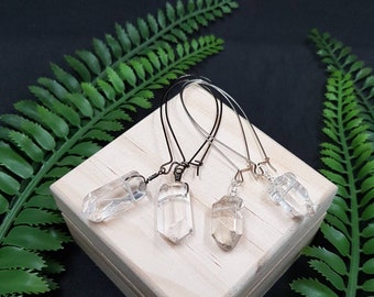 Puede incluir: Tres pares de pendientes de cristal con bucles de alambre. Los cristales son transparentes y facetados. Los pendientes se muestran en una caja de madera con un fondo de hojas verdes.
