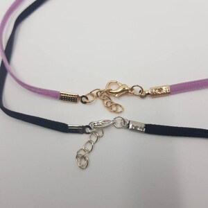 May include: Two delicate ribbon chokers with gold and silver clasps. The top choker is lavender and the bottom choker is black.