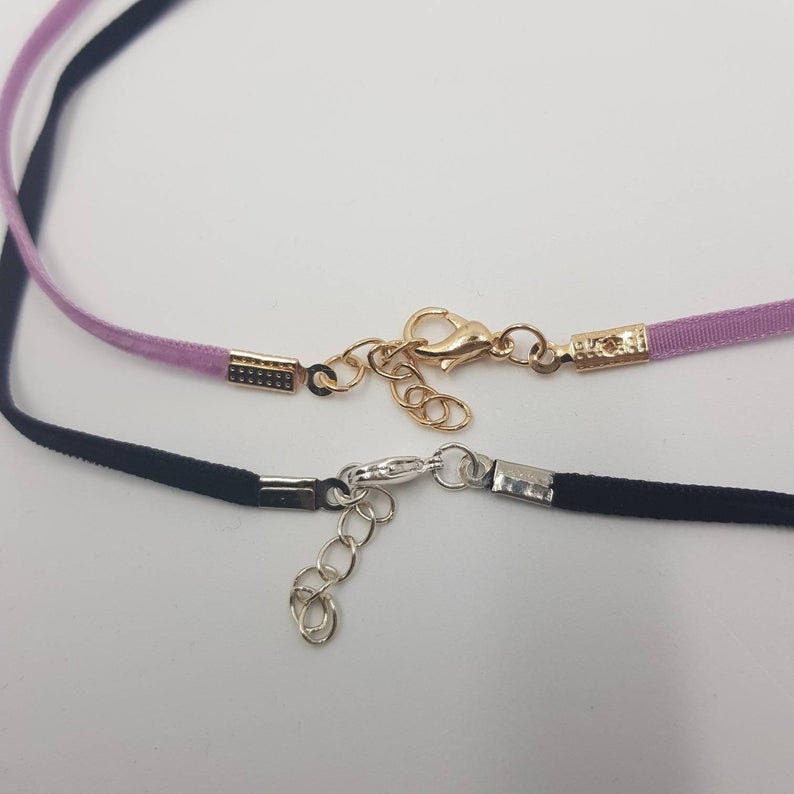 May include: Two delicate ribbon chokers with gold and silver clasps. The top choker is lavender and the bottom choker is black.
