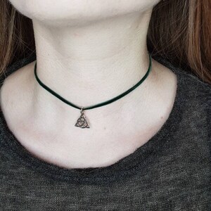 May include: A black choker necklace with a silver pendant in the shape of a Celtic knot. The pendant is about 1 inch in diameter.