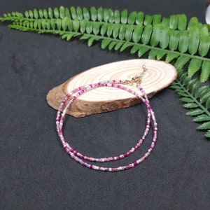 Könnte beinhalten: Eine zarte Halskette aus rosa und weißen Perlen mit einem goldenen Verschluss. Die Halskette ist mehrlagig und besteht aus kleinen, runden Perlen.