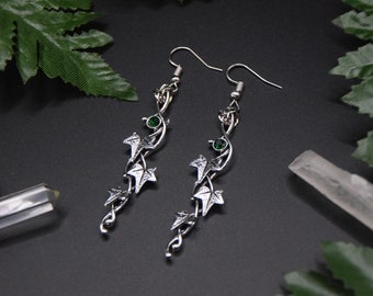 May include: A pair of silver earrings with a vine design and green gemstones. The earrings are long and dangle.