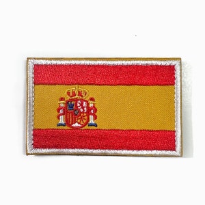 May include: Embroidered patch featuring the flag of Spain. The rectangular patch has a gold center stripe, flanked by red stripes at the top and bottom. The Spanish coat of arms is centered on the gold stripe, with a silver border.