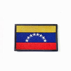 May include: Rectangular patch featuring the flag of Venezuela. The flag design includes a yellow stripe at the top, a blue stripe in the middle with seven white stars, and a red stripe at the bottom. The patch has a black border.