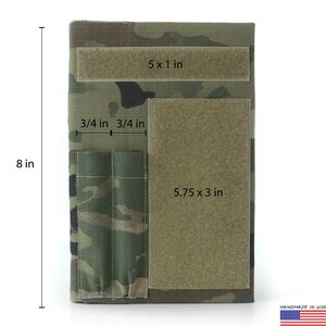 May include: A camouflage-patterned notebook cover, 8 inches tall and 5.5 inches wide, with three hook-and-loop patches of varying sizes. Includes two pen holders and the text "HANDMADE IN USA By L'FEME".