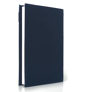 May include: A navy blue book with a textured cover stands upright against a white background. The book's spine is visible, revealing white pages. The cover is a solid, dark blue color.