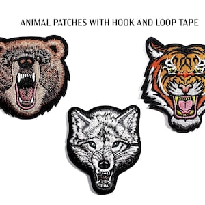 Peut inclure: Écussons brodés d'animaux avec du velcro. L'image montre un ours brun, un tigre avec des rayures orange et noires, et un loup gris, tous avec la gueule ouverte et les dents visibles.