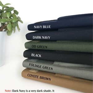 May include: A stack of fabric samples in various colors, including Navy Blue, Dark Navy, OD Green, Black, Foliage Green, and Coyote Brown. Each sample has a label with its color name. The text at the bottom states that Dark Navy is a very dark shade.