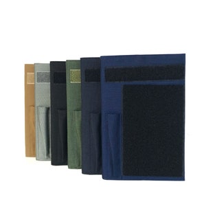 May include: A row of fabric pouches in various colors, including tan, gray, black, olive green, navy blue, and dark blue. Each pouch features a Velcro closure and a smaller pocket. The pouches are designed for storage and organization.