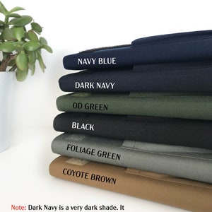 May include: A stack of fabric samples in various colors, including Navy Blue, Dark Navy, OD Green, Black, Foliage Green, and Coyote Brown. Each sample has a label with its color name. The text at the bottom says, "Dark Navy is a very dark shade. It looks almost like black."