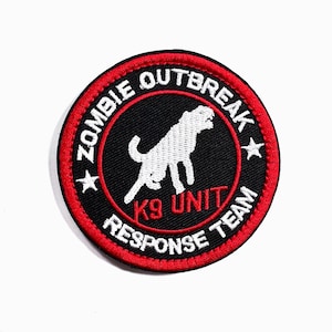 May include: Embroidered patch with a black background and a red border. The patch features the text "ZOMBIE OUTBREAK RESPONSE TEAM K9 UNIT" in white. A white silhouette of a dog is in the center.