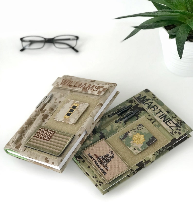 May include: Two camouflage-patterned notebooks with personalized name patches. One notebook features an American flag patch and the name "WILLIAMS." The other notebook displays the name "MARTINEZ" and a "Don't Tread on Me" patch. Both have pen holders.