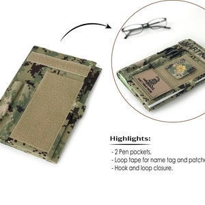 May include: A camouflage-patterned notebook cover with a hook and loop closure. Features two pen pockets and loop tape for name tags and patches. The cover is open, revealing a notebook with a name tag that reads "MARTINEZ" and a patch that reads "DON'T TREAD ON ME".