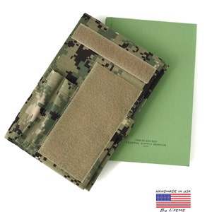 May include: A camouflage pattern notebook cover with hook and loop fasteners, next to a green notebook. The cover is made of a digital camouflage fabric. The text "7530-00-222-3521 FEDERAL SUPPLY SERVICE (FSC)" is visible on the green notebook. "HANDMADE IN USA" is also visible.