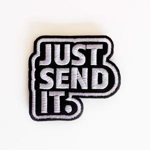 May include: Black and white embroidered patch with the text "JUST SEND IT" in a bold, stylized font. The patch has a black border and a white background for the text, creating a high-contrast design. The patch is rectangular with rounded corners.