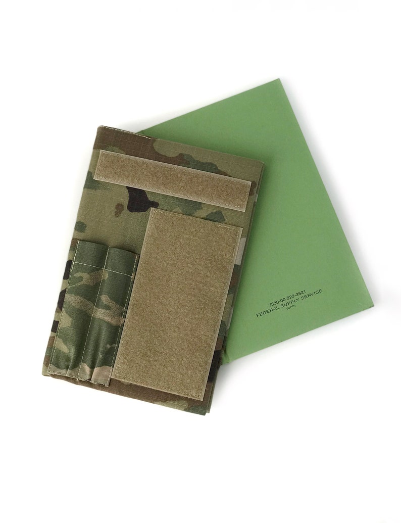 May include: A camouflage-patterned tactical notebook cover with hook and loop closures and pockets, paired with a green document. The document has the text "FEDERAL SUPPLY SERVICE".