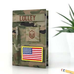 May include: Camouflage-patterned notebook with a pen holder, name patch, and military insignia. Features an American flag patch. The name "LOLLEY" is embroidered on a rectangular patch above the insignia.