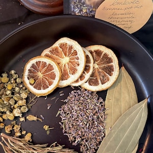 May include: A black bowl containing dried ingredients for a simmer pot kit, including dried lemon slices, lavender buds, chamomile flowers, rosemary sprigs, and bay leaves. A label reads: Emsole Simmer pot kit lavender chamomile rosemary lemon leaf.