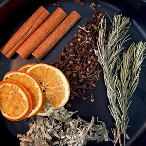 May include: A collection of dried ingredients arranged on a black surface, including three brown cinnamon sticks, a pile of dark brown cloves, three dried orange slices, a cluster of dried green herbs, and three sprigs of fresh green rosemary.