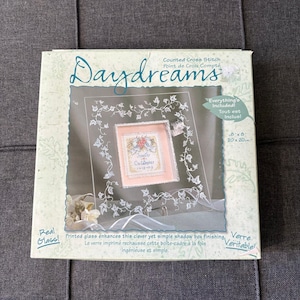 Puede incluir: Un kit de punto de cruz contado Daydreams en una caja cuadrada. El empaque presenta un gráfico de un proyecto terminado con un borde floral y los nombres Jennifer y Christopher con la fecha 12-12-02. Mide 20 cm por 20 cm.