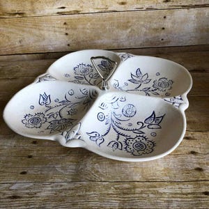 May include: White ceramic serving dish with four sections and a silver handle. The dish is decorated with blue floral patterns. The dish is on a wooden surface.