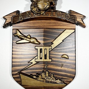 Könnte beinhalten: Eine hölzerne Wandplakette mit dem ANGLICO-Emblem und einem goldfarbenen Marine Corps Adler, Globus und Ankerwappen an der Spitze. Der Schild zeigt ein goldenes Flugzeug, eine römische Ziffer III, einen Blitz und ein Schiff mit Fallschirm.