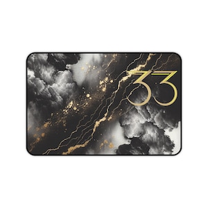 May include: A rectangular desk mat featuring a black and white smoky, cloud-like background with a diagonal gold-colored vein pattern. The number 33 is printed in a large, gold-colored font on the right side of the mat with a black border.