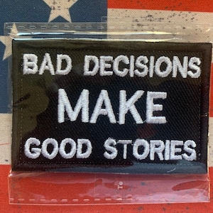 May include: Black patch with white embroidered text that reads "Bad Decisions Make Good Stories".