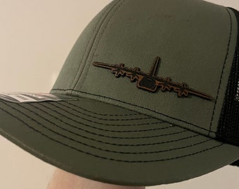 Könnte beinhalten: Eine grüne und schwarze Trucker-Kappe mit einem braunen Leder-Flugzeug-Patch auf der Vorderseite.