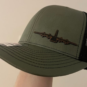Peut inclure: Un chapeau de camionneur vert et noir avec un patch d'avion en cuir marron sur le devant.