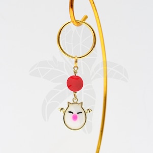 May include: A gold charm with a white and pink cartoon character with wings, a red bead, and a gold ring.
