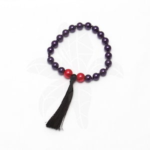 May include: A purple beaded bracelet with a black tassel and two red beads.