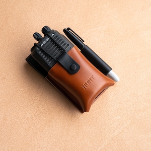 Könnte beinhalten: Ein braunes Leder-Funkgerät-Etui mit einem schwarzen Motorola-Funkgerät und einem schwarzen Stift im Inneren. Das Etui trägt den Schriftzug "HUNT" auf der Vorderseite.
