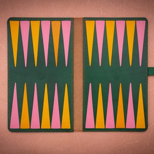 May include: A green backgammon board with a colorful design. The board features alternating pink and yellow triangles on each side. The board is closed and has a green strap with a snap closure.