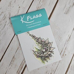 Pode incluir: Um decalque &agrave; prova de intemp&eacute;ries com uma ilustra&ccedil;&atilde;o detalhada de um esqueleto de criatura cercado por flores e folhagem. O decalque &eacute; embalado em um envelope branco com um cabe&ccedil;alho turquesa que diz "K. FLAGG Art and Illustration 1 Weatherproof Decal".