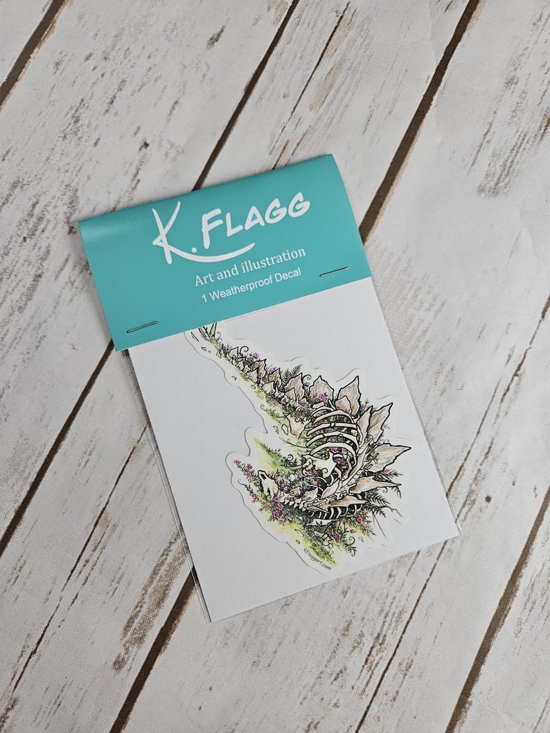 Pode incluir: Um decalque &agrave; prova de intemp&eacute;ries com uma ilustra&ccedil;&atilde;o detalhada de um esqueleto de criatura cercado por flores e folhagem. O decalque &eacute; embalado em um envelope branco com um cabe&ccedil;alho turquesa que diz "K. FLAGG Art and Illustration 1 Weatherproof Decal".