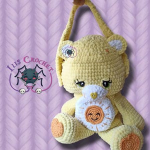 Puede incluir: Bolso de oso de ganchillo amarillo hecho a mano con un bolsillo en forma de sol blanco y naranja. El oso tiene una cara sonriente, ojos verdes y un asa larga. El bolso tiene un logotipo que dice "Ius Crochet" con una ilustración de araña.
