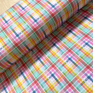 May include: A roll of colorful plaid fabric. The pattern features intersecting lines in shades of pink, blue, green, yellow, and orange. The fabric is tightly rolled, with the pattern visible on the surface.