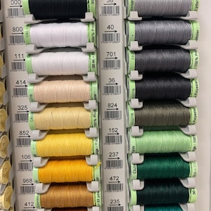 May include: A close-up of two rows of spools of thread, each with a different colour. The spools are arranged in a grid pattern, with the numbers 000, 800, 1111, 414, 325, 852, 106, 968, 412, 350 on the left side and 38, 40, 701, 36, 824, 152, 237, 472, 235, 143 on the right side. The spools are all the same size and shape, and they are all made of the same type of thread.