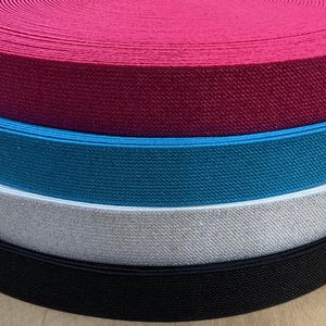 Puede incluir: Cuatro rollos de tejido elástico en diferentes colores: negro, blanco, azul verdoso y burdeos. El elástico está doblado y apilado uno encima del otro.