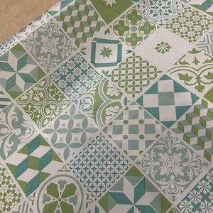 May include: A patterned surface with a repeating design of geometric shapes in shades of green and teal on a white background. The design includes squares, diamonds, and other shapes with floral and geometric patterns.